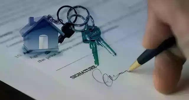 Foto Schriftstück, Unterschrift wird getätigt, Schlüssel liegen darauf mit Schlüsselanhänger in Hausform